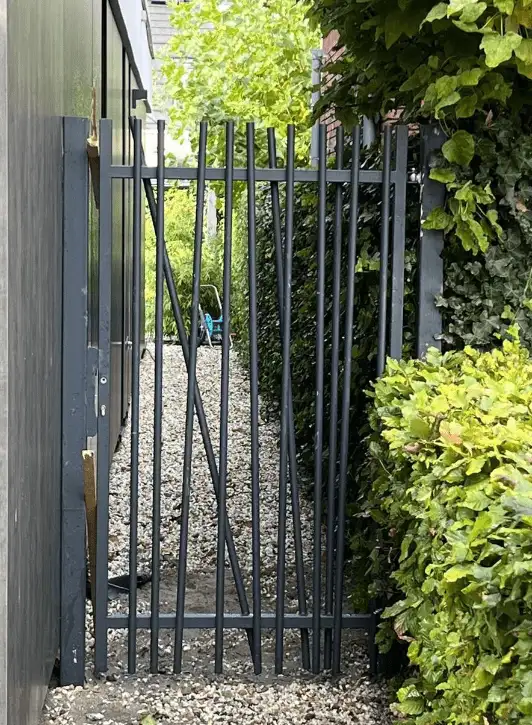 Stalen looppoort met kriskras-spijlen naast een woning