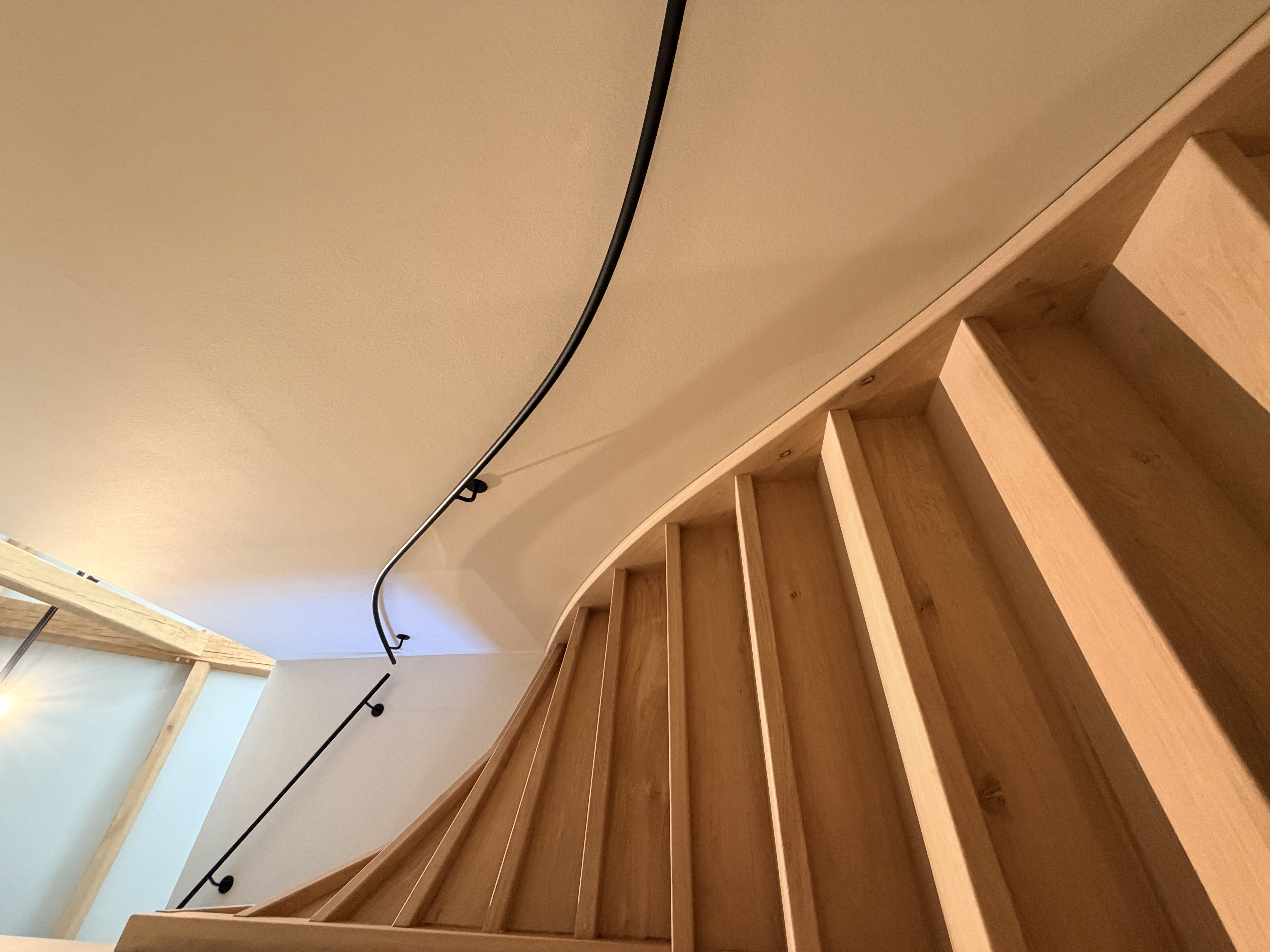 S-Gravenzande stalen trapleuning: perspectief van de trapopgang met de zwarte maatwerk leuning, detail van de montage op de lichte muur