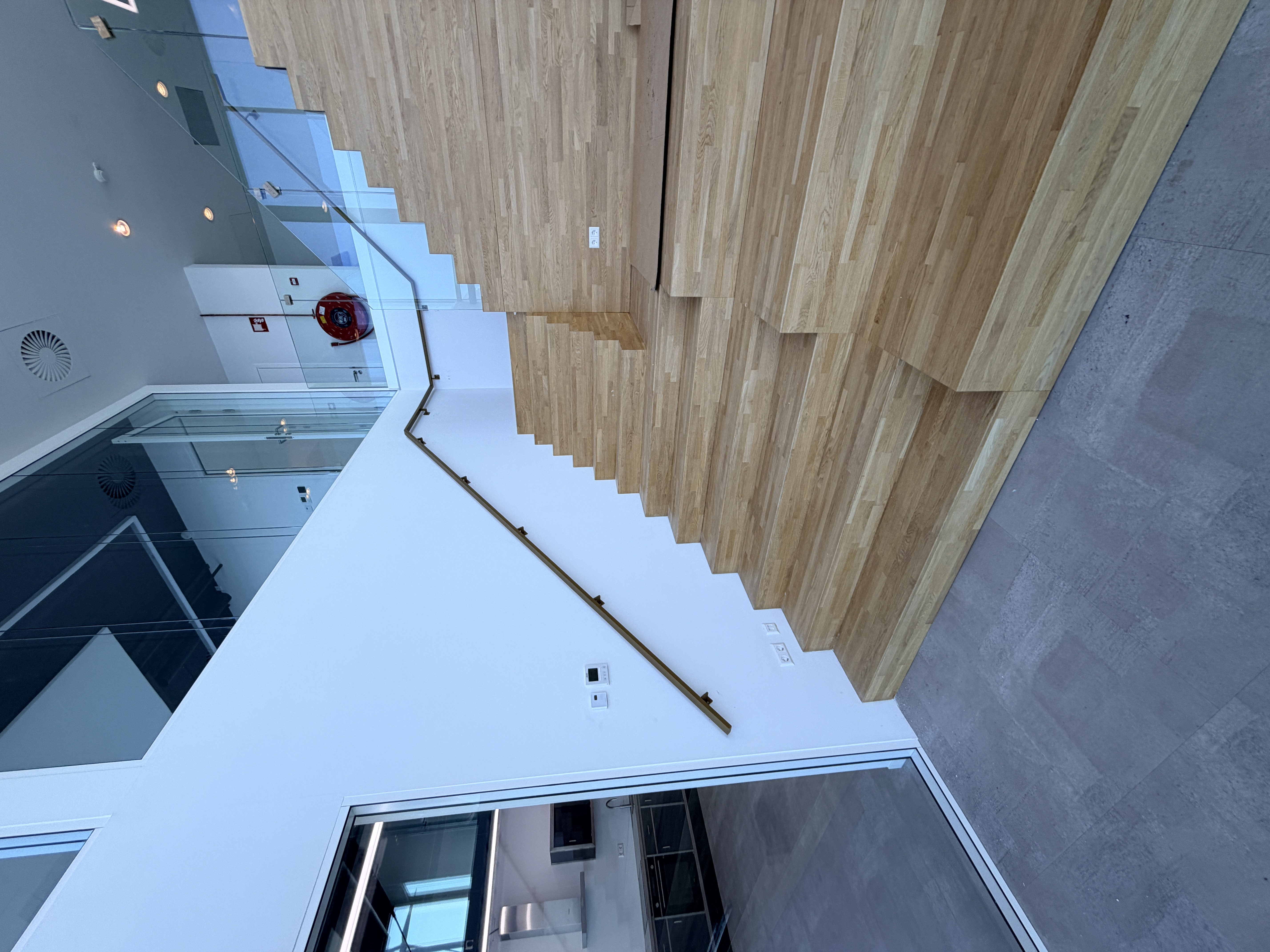 Goud gecoate stalen trapleuning in modern kantoorpand te Rotterdam, lange uitzicht langs houten trap en glazen balustrade